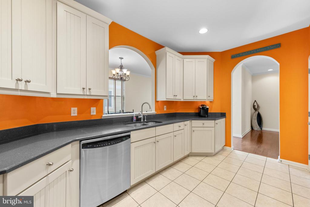 Kitchen with white cabinets, dark countertops, stainless dishwasher, and vivid orange walls.