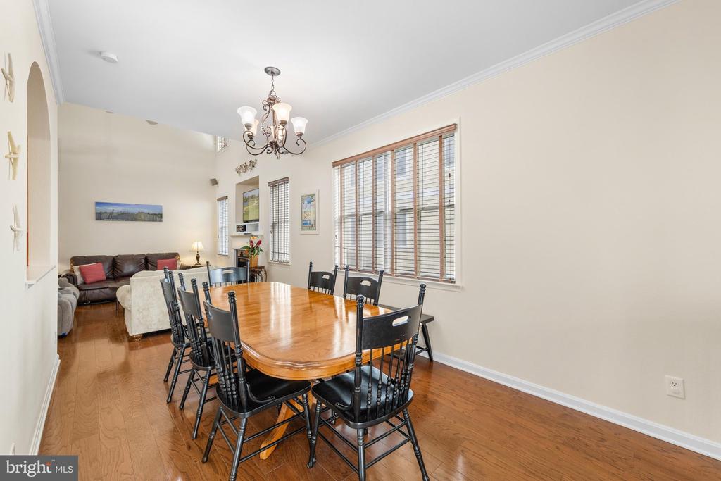 Dining room with a wooden table and black chairs beside windows, opening to living room.
