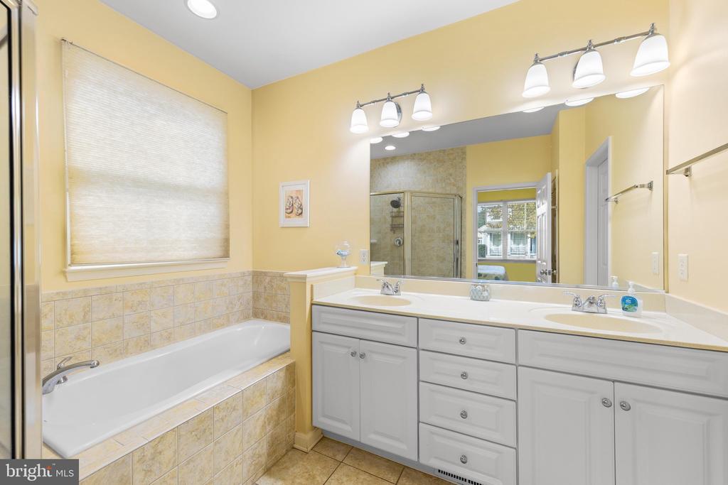 Bathroom with a tiled bathtub and long double-sink vanity beneath a large mirror.