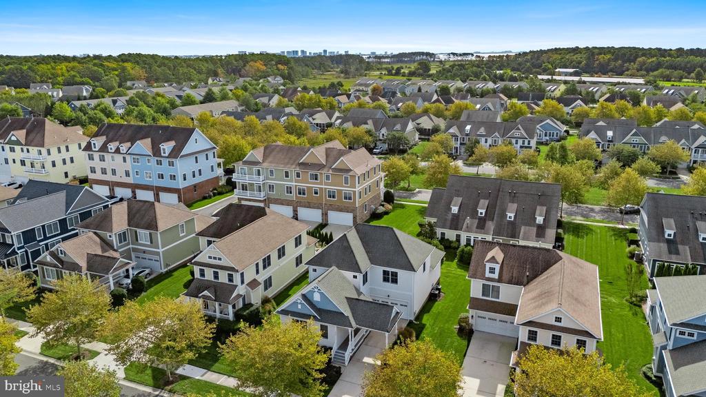 Aerial view of a residential neighborhood with closely spaced homes, green lawns, and woods on the horizon.