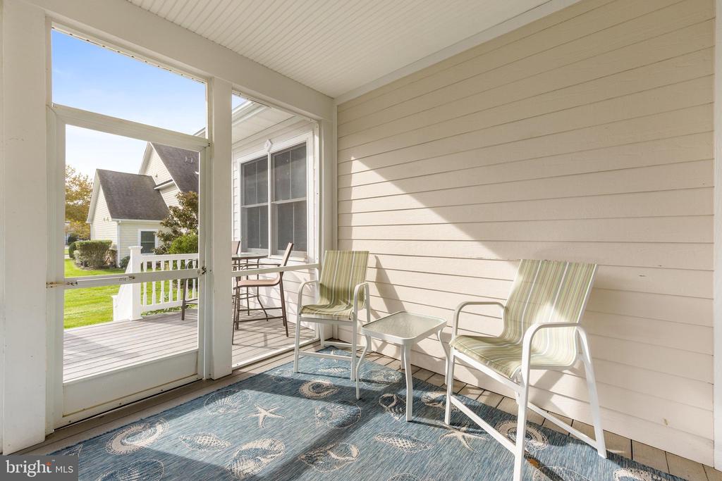 Screened porch with two striped chairs, a small table, and a blue patterned rug.