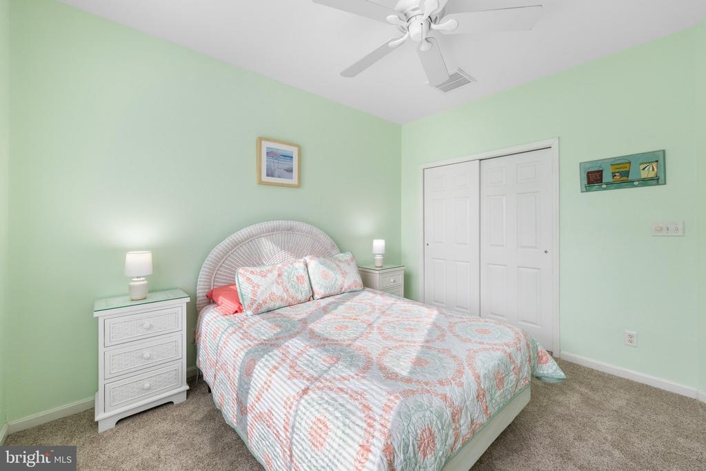 Bedroom with a patterned bedspread, mint-green walls, and a white ceiling fan.