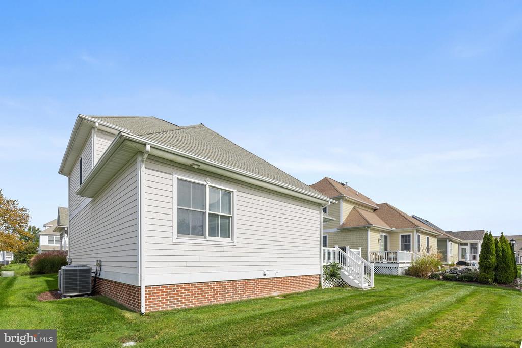 Side view of a light-sided home with a brick foundation and neatly mown lawn.