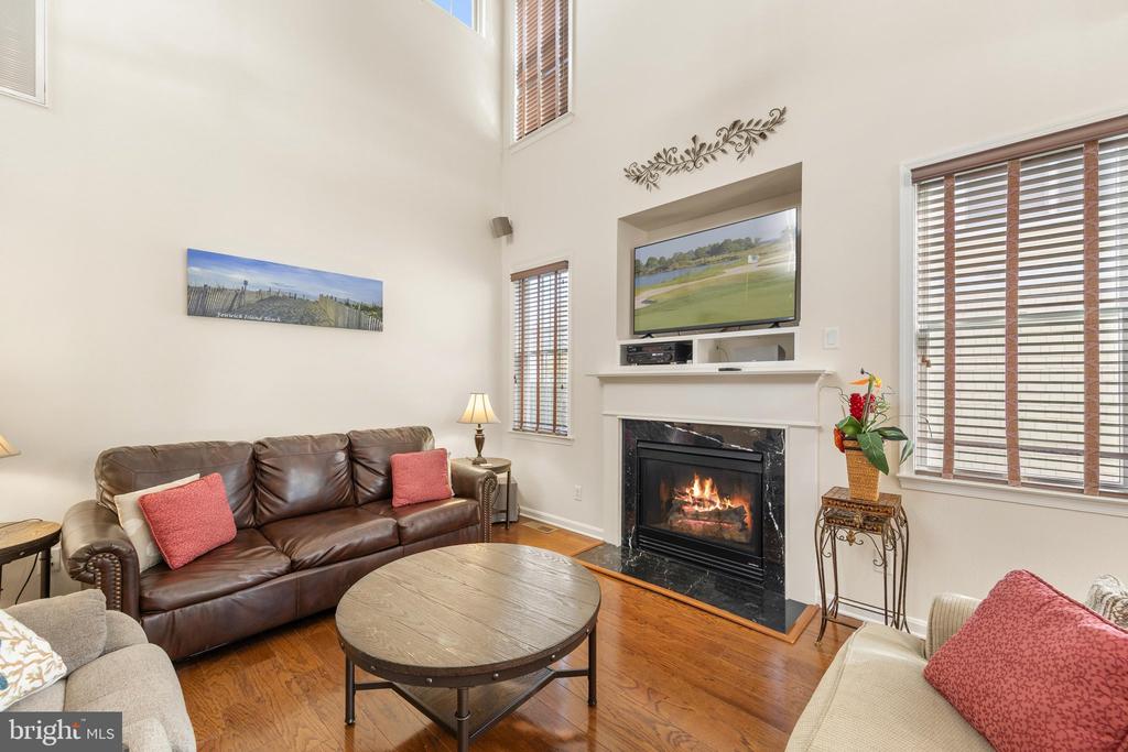 Vaulted living room with a leather sofa, hardwood floors, and a fireplace beneath a television.