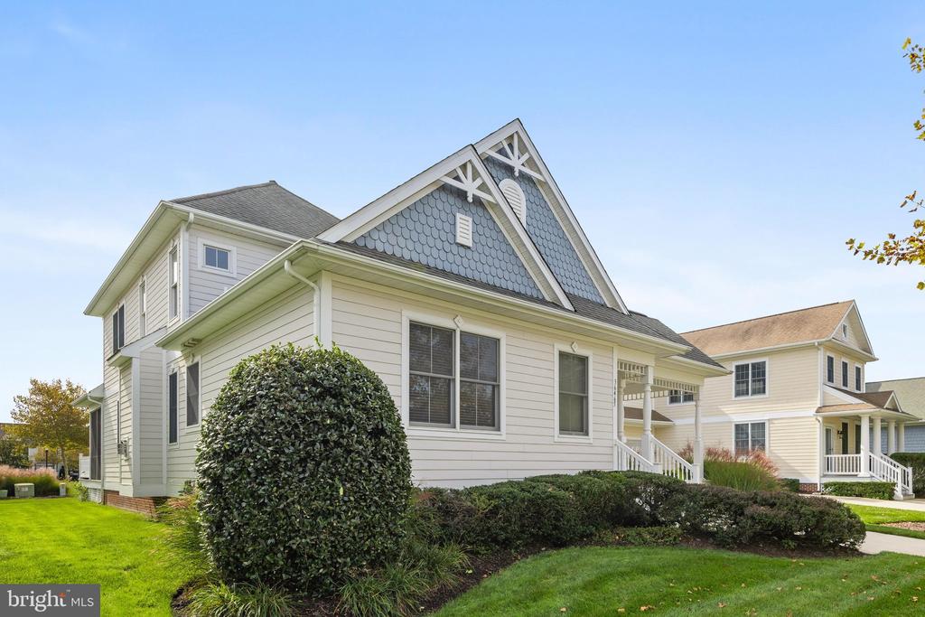 Light-sided home with a blue-gray gabled roof, white porch, and landscaped lawn.