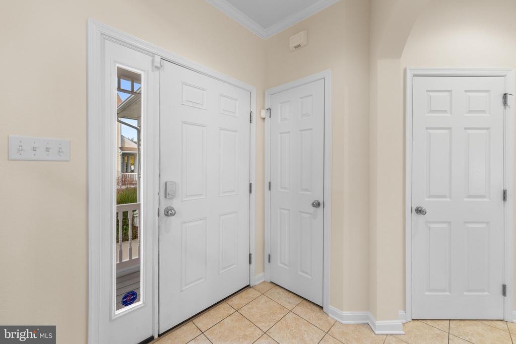 Entryway with a white front door, narrow sidelight, tiled floor, and two interior doors.
