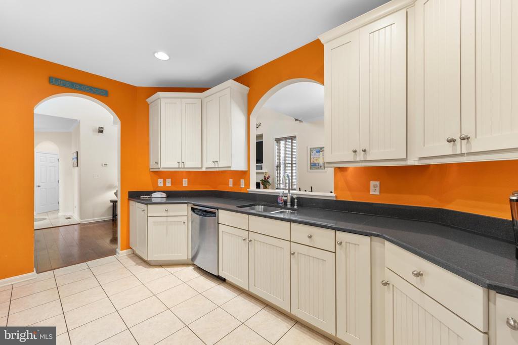 Kitchen with white cabinets, dark countertops, orange walls, and a stainless steel dishwasher.