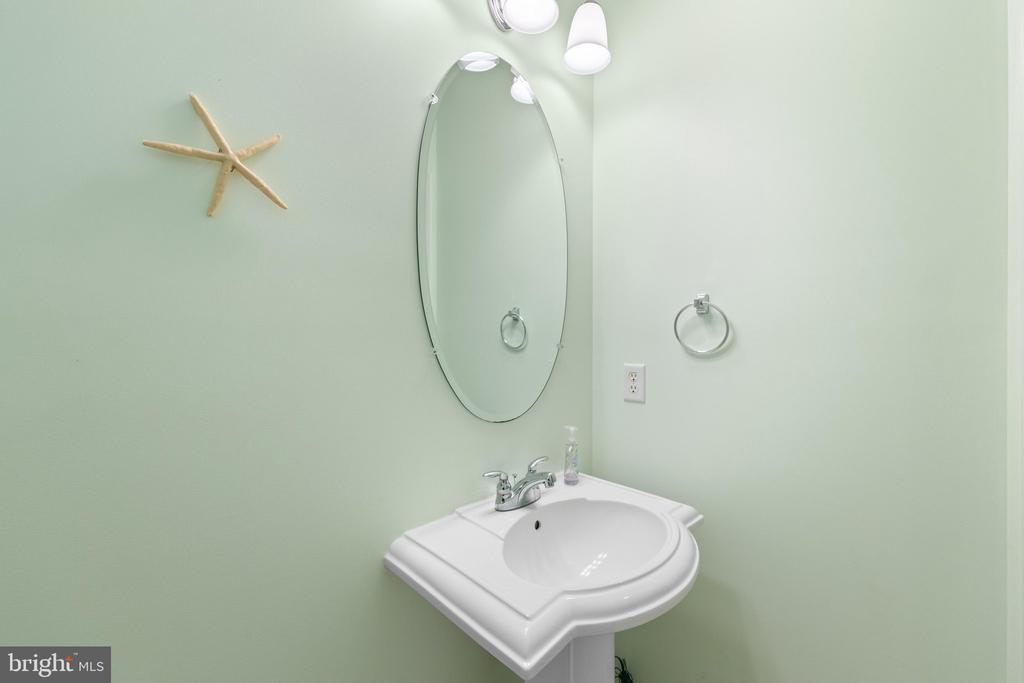 Bathroom with a white pedestal sink, oval mirror, and pale green walls.