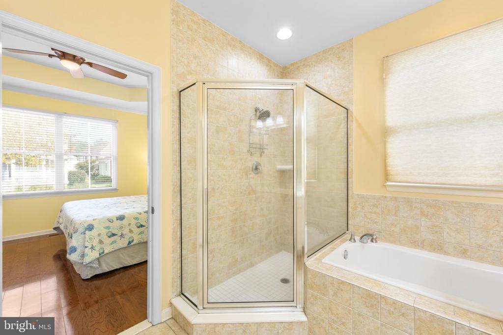 Bathroom with a glass-enclosed shower and bathtub beside a bedroom with a large window.