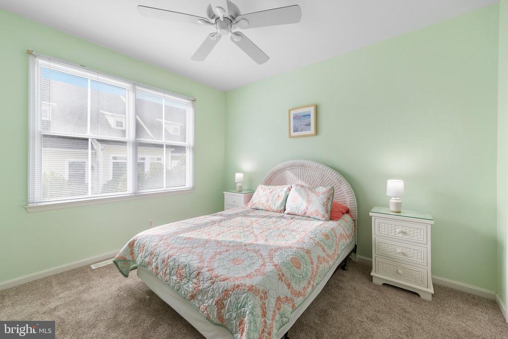 Bedroom with a floral quilt, pale green walls, and wide windows with blinds.