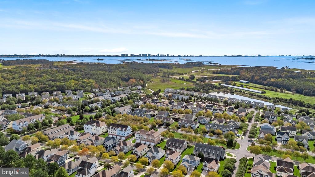 Aerial view of a coastal neighborhood with homes, wooded areas, and water on the horizon.