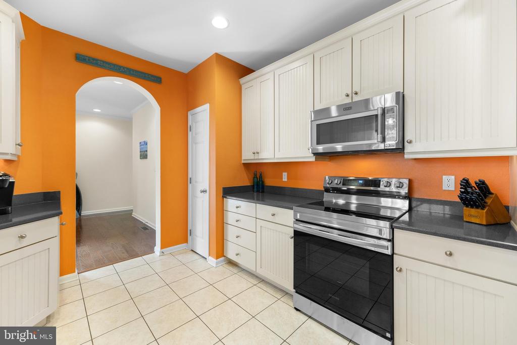 Kitchen with white cabinets, stainless steel appliances, dark counters, and bright orange walls.
