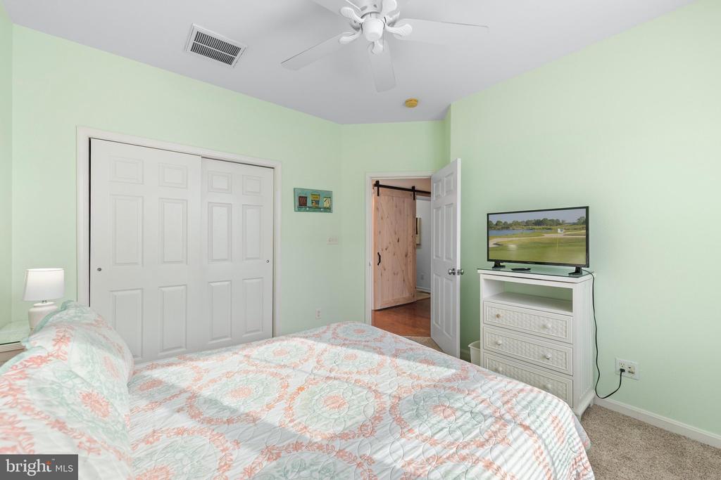 Bedroom with a patterned quilt, white closet doors, and a television on a dresser.