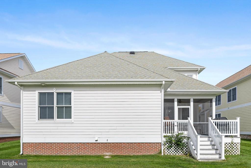 Rear exterior of a light-sided home with a screened porch, white-railed steps, and a brick foundation.