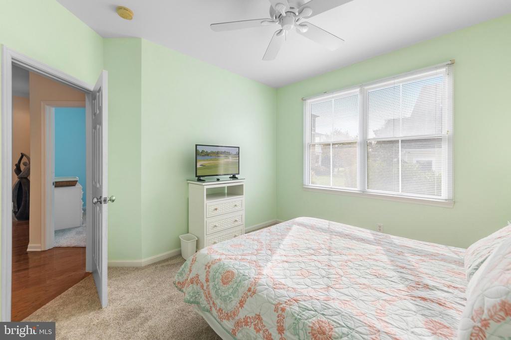 Bedroom with a patterned quilt, pale green walls, and a wide window with blinds.