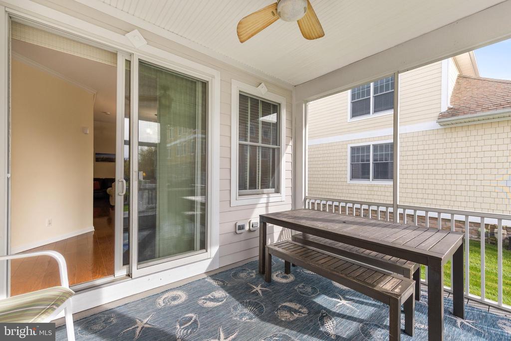 Covered screened porch with a ceiling fan, blue patterned rug, and dark outdoor table.