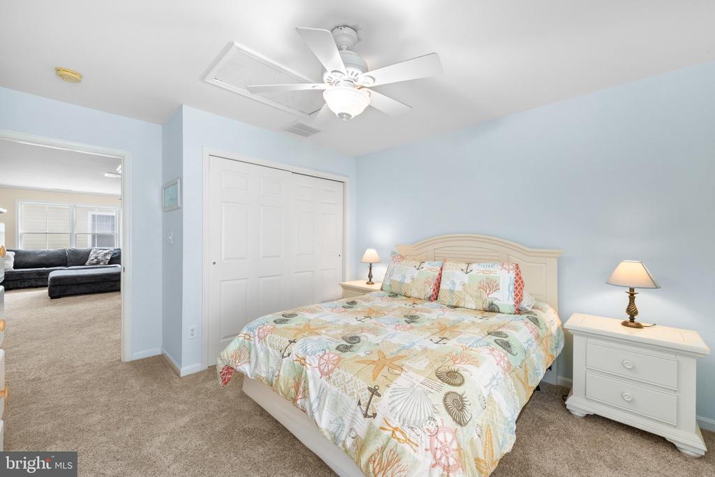 Bedroom with a colorful seashell-patterned bedspread, white furniture, and an open doorway to the living room.