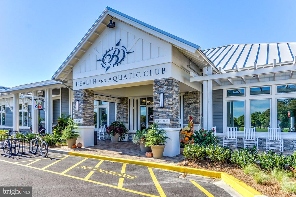 Health and Aquatic Club clubhouse with stone columns, white chairs, and a striped metal roof.