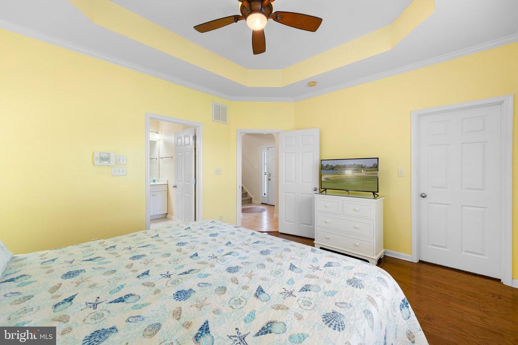 Bedroom with a patterned bedspread, yellow walls, ceiling fan, and white dresser with a television.