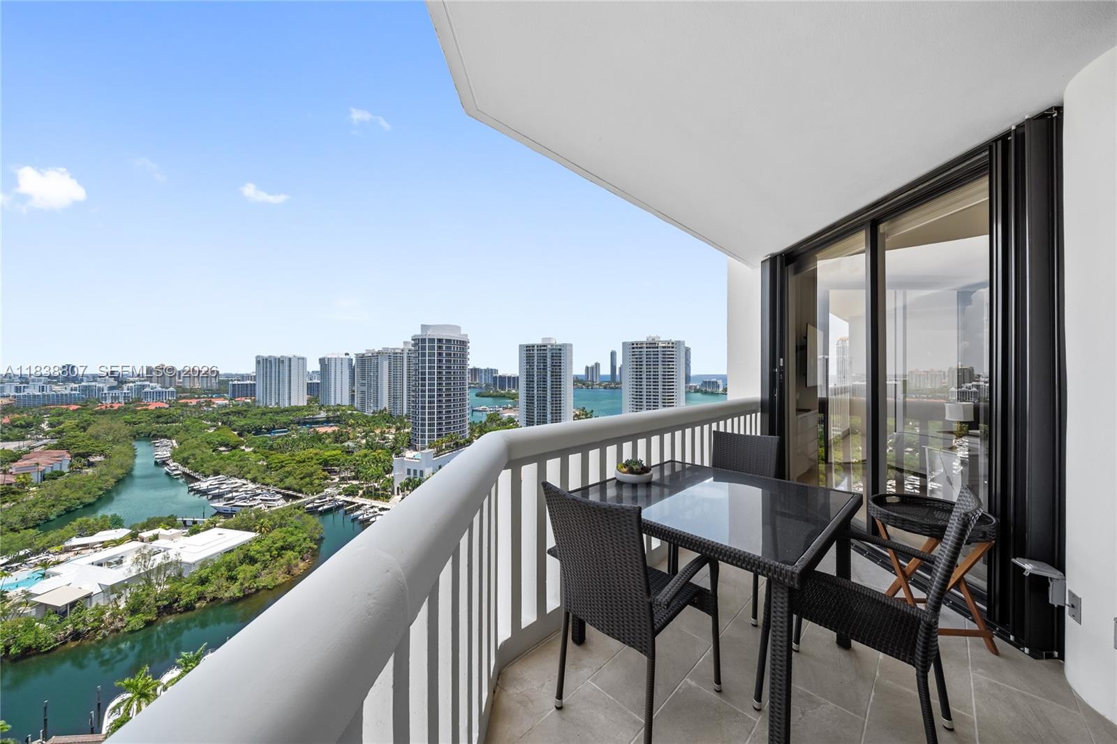 Furnished condo balcony overlooking a turquoise waterway, marina, and waterfront skyline.