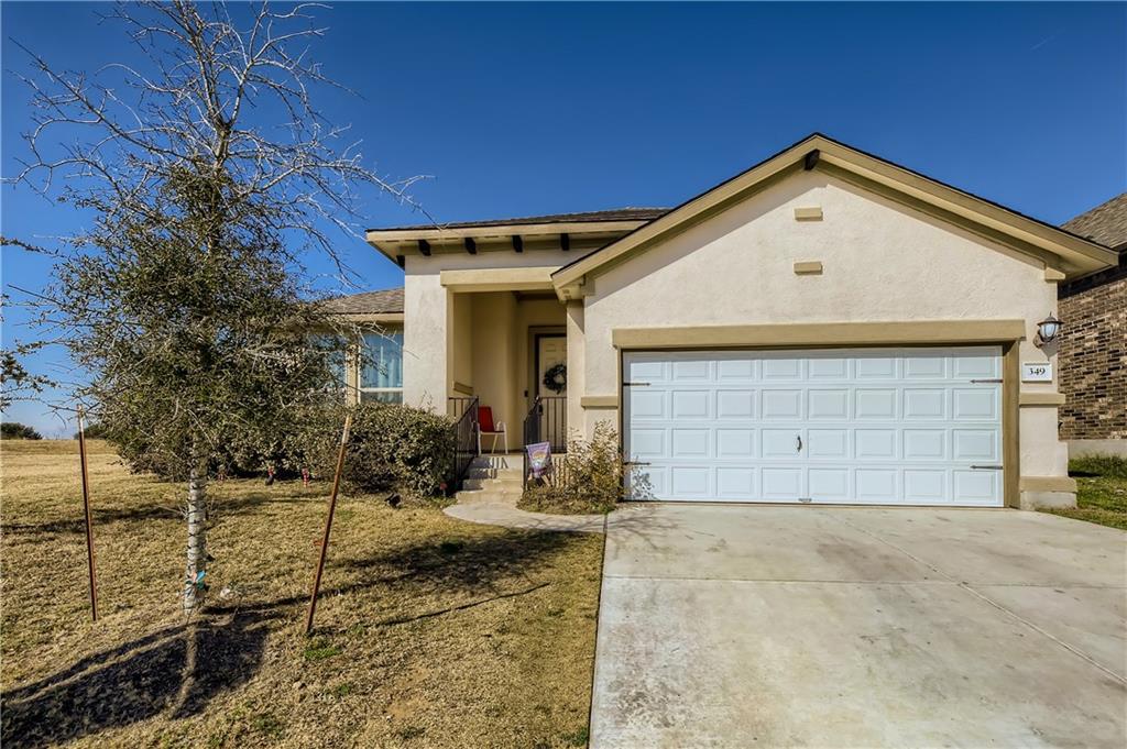 Single-story stucco house with a two-car garage, covered entry, and leafless tree.