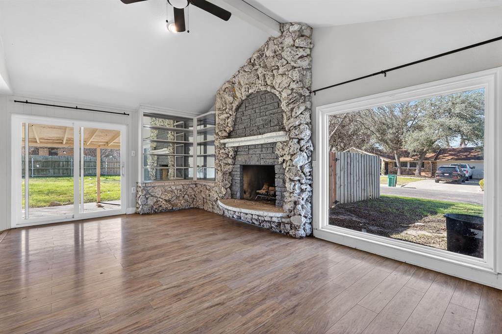 Vacant living room with a prominent stone fireplace and wide windows overlooking the yard.