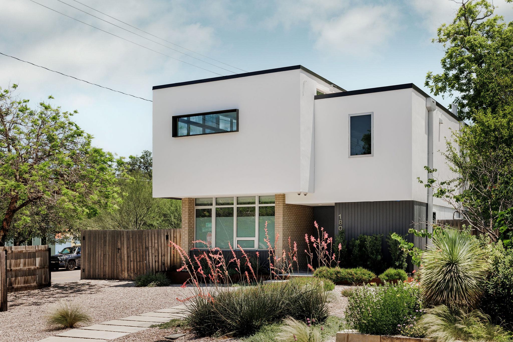 Modern white house with geometric volumes, a flat roof, and drought-tolerant landscaping.