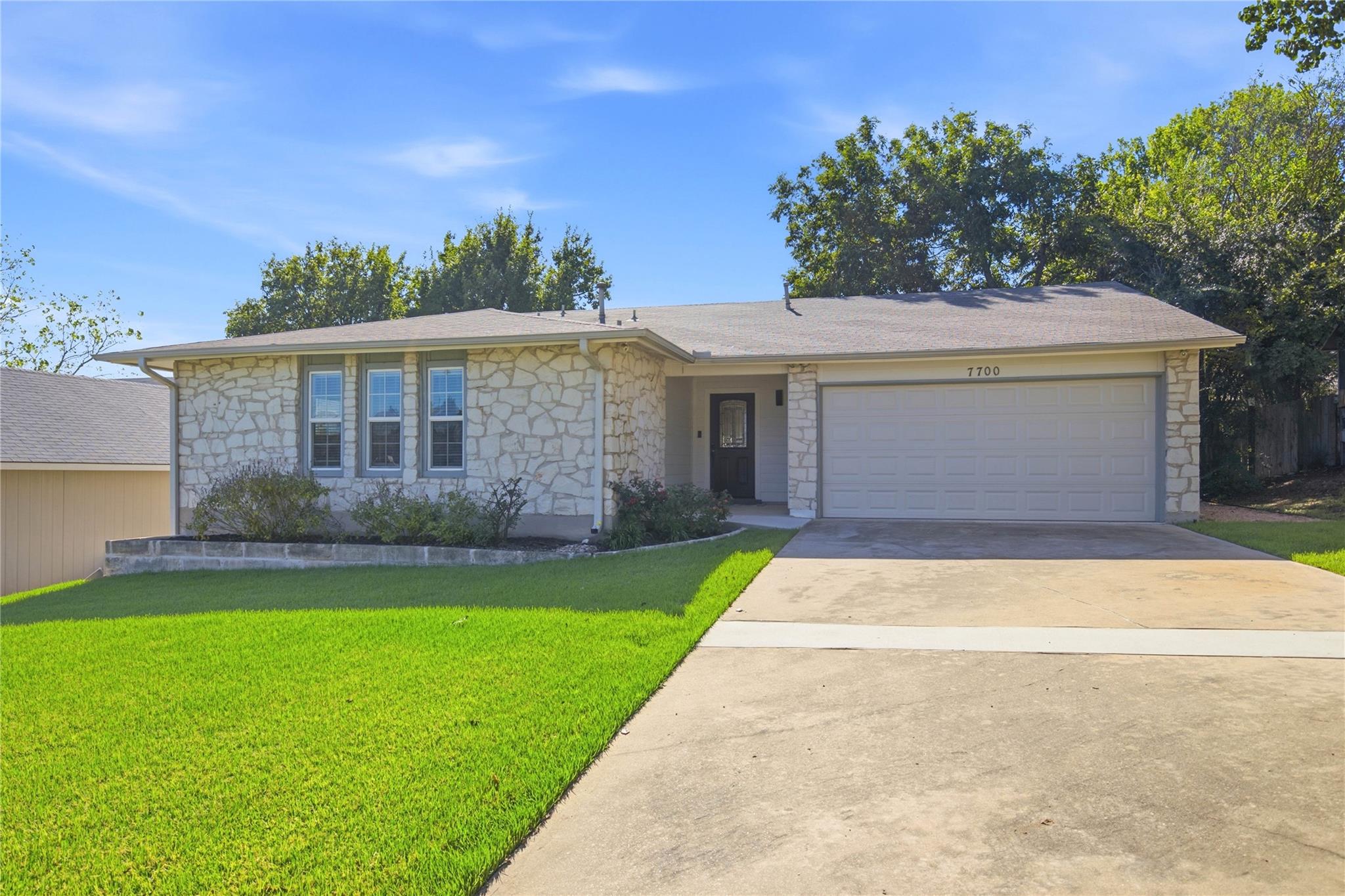 Single-story stone-faced home with a two-car garage, broad driveway, and green lawn.