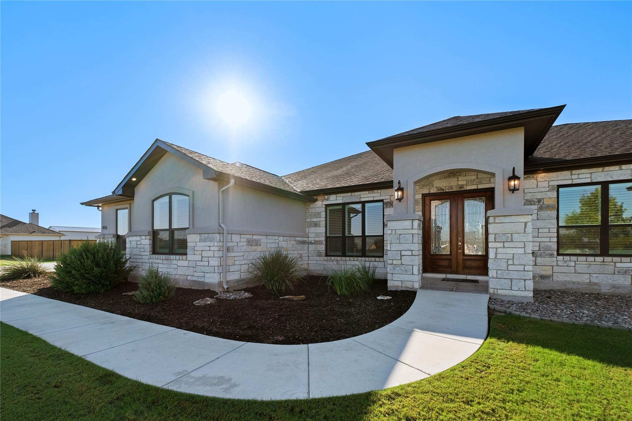 Stone-and-stucco house with wooden double doors, landscaped beds, and a curved front walkway.