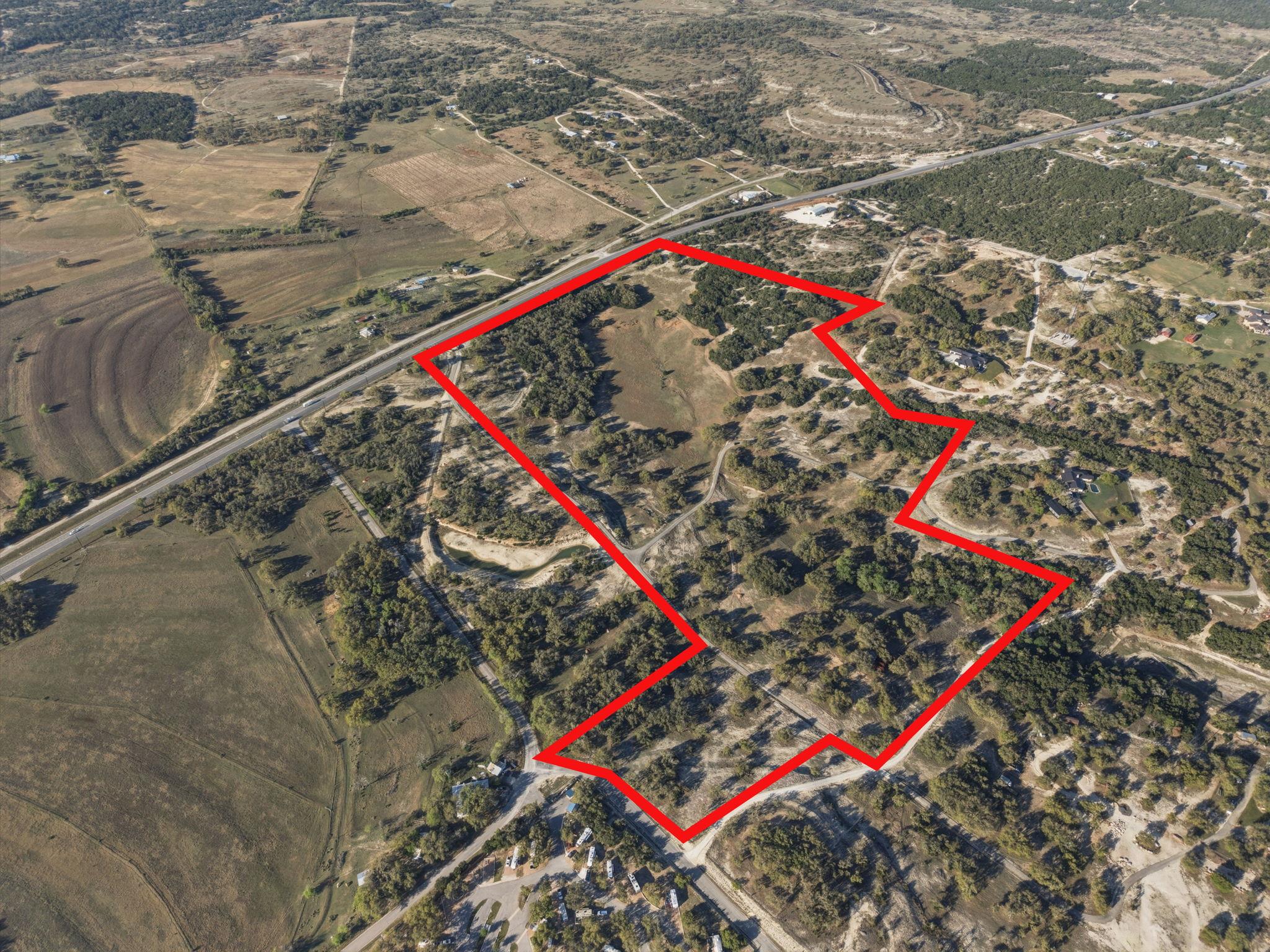 Aerial view of a rural tract outlined in red, with scattered trees and a highway along one edge.