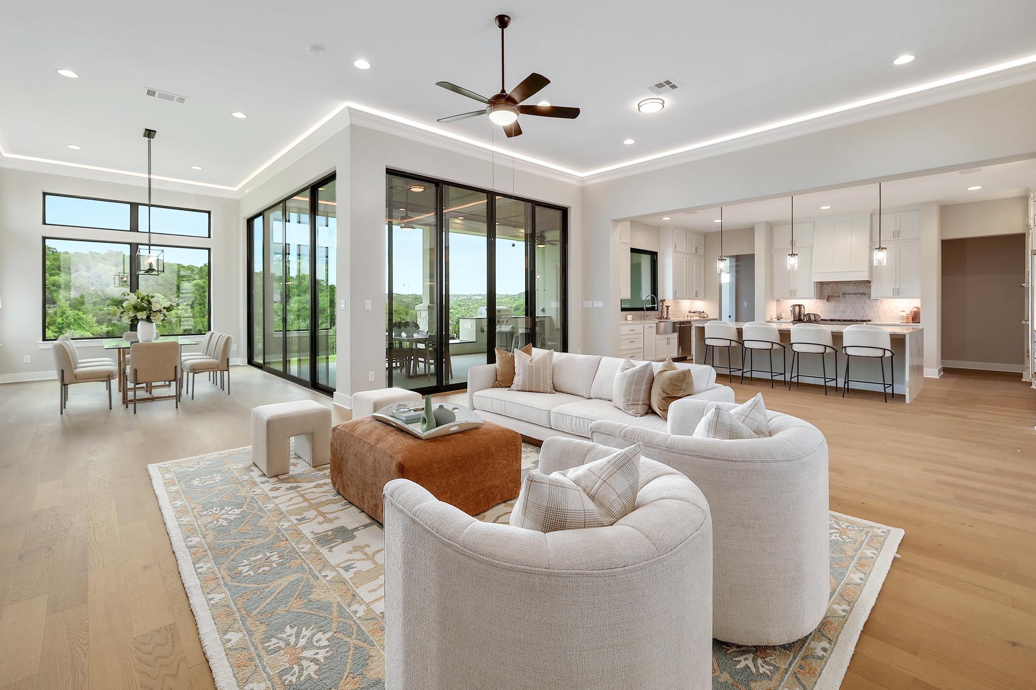 Open-plan living room with curved cream sectional, large glass doors, dining area, and white kitchen.