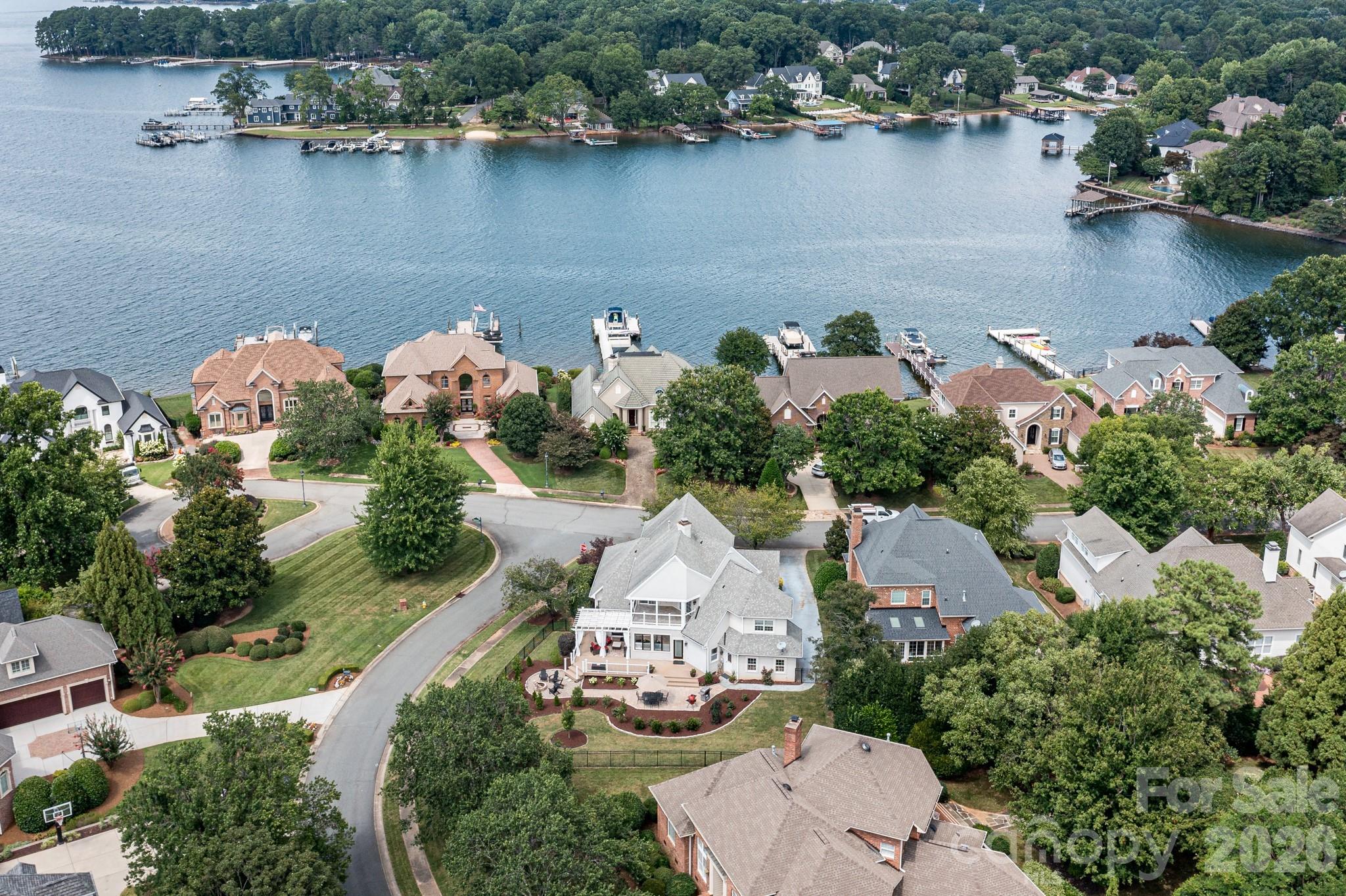 Aerial view of lakefront homes with private docks and boats along a wooded shoreline.