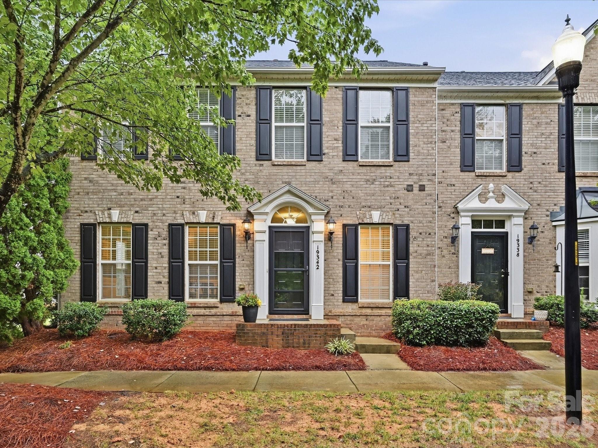 Two-story brick townhomes with dark shutters, white entry trim, and landscaped front beds.