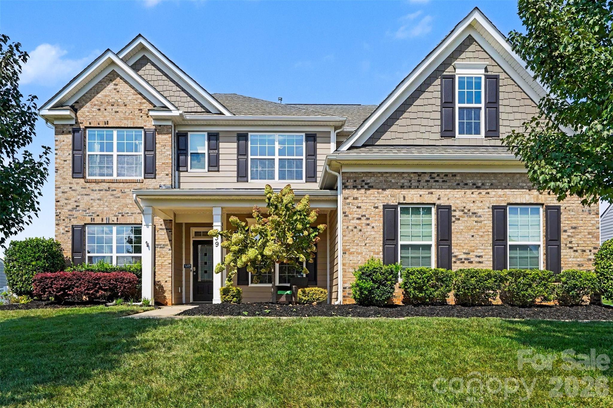Two-story brick and siding home with multiple gables, dark shutters, and a landscaped front lawn.