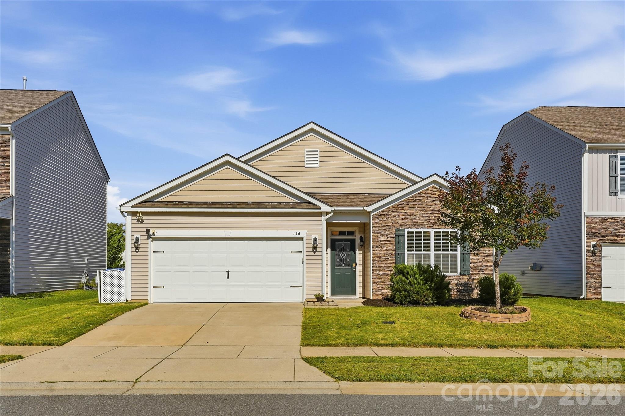 Front exterior of a beige home with stone accents, a two-car garage, and a landscaped lawn.