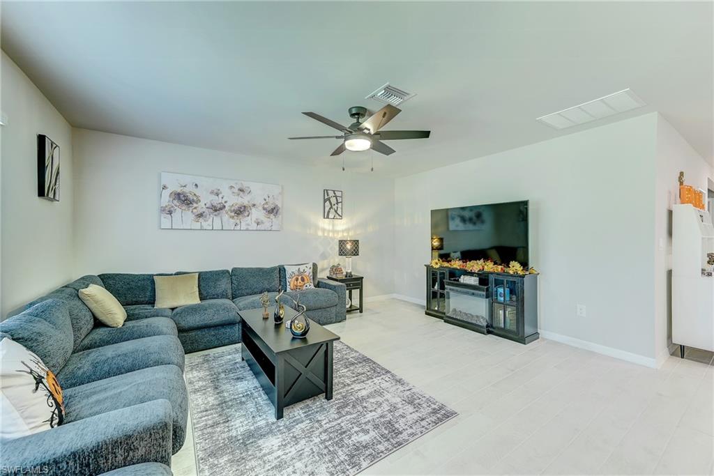 Living room with a blue-gray sectional sofa, television, patterned rug, and white tile floor.