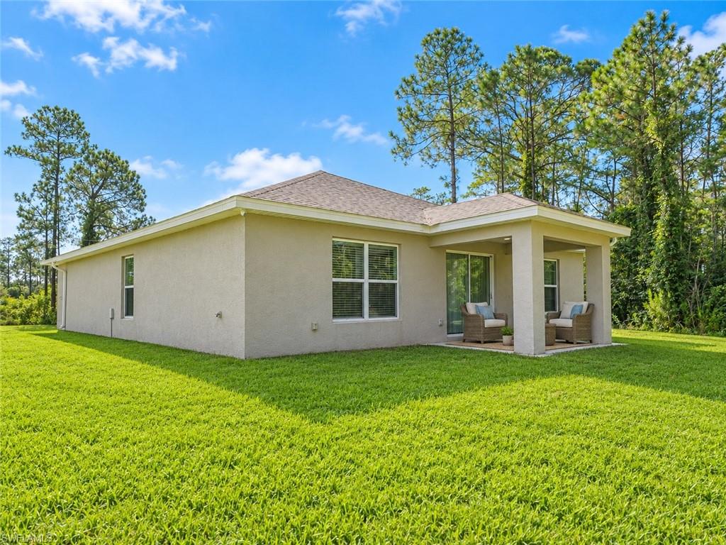 Single-story stucco home with a covered patio, two chairs, and a wide green lawn.