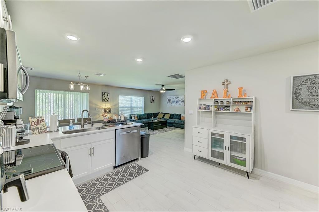 Open kitchen with white cabinetry and sink island adjoining a living room with a teal sectional.
