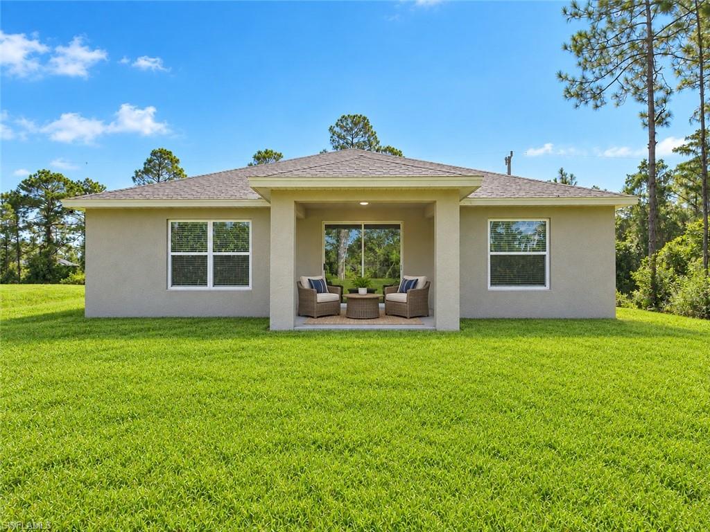 Single-story stucco home with a covered patio, outdoor seating, and a broad green lawn.
