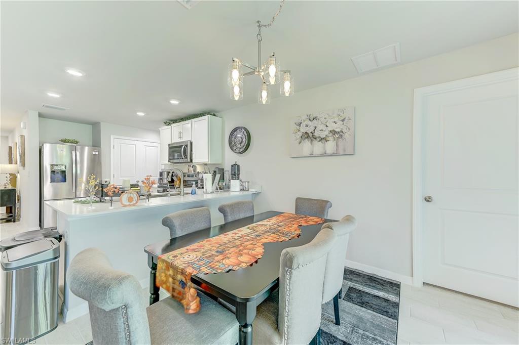 Dining area with gray upholstered chairs, an orange table runner, and an adjoining white kitchen.