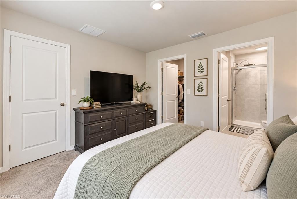 Staged bedroom with a white bed, green throw, dark dresser, and adjoining closet and shower.