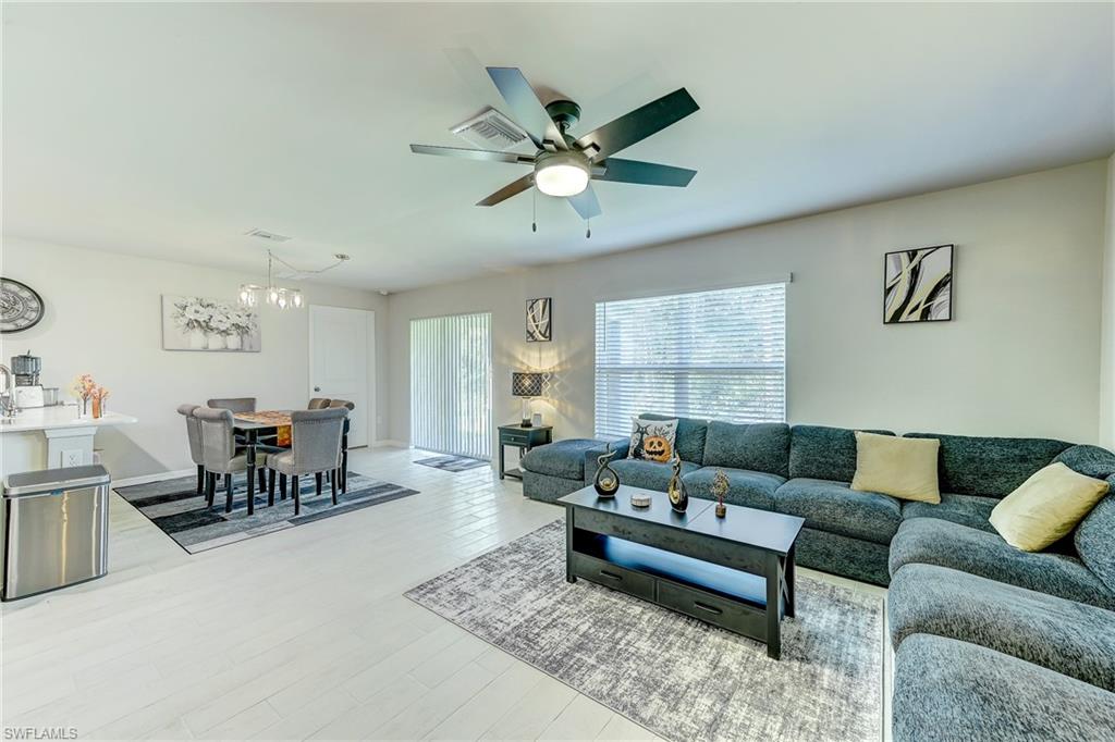 Open-plan living and dining area with a gray sectional, large windows, and a ceiling fan.