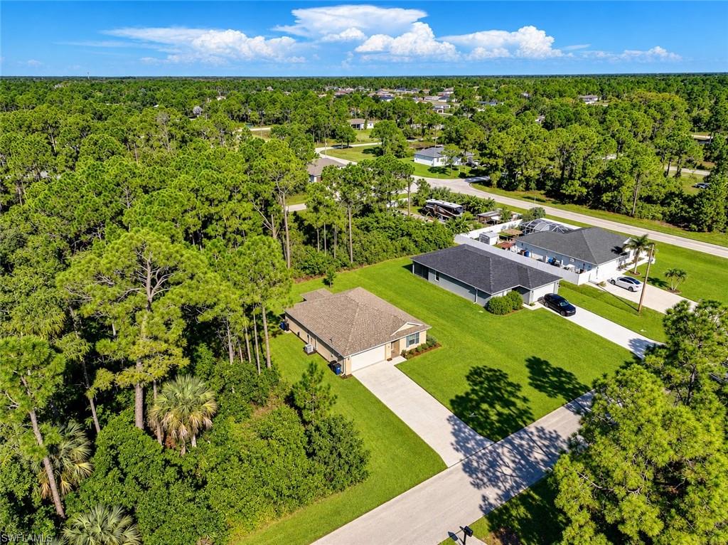 Aerial view of a single-story home, driveway, broad lawn, and surrounding pine woodland.