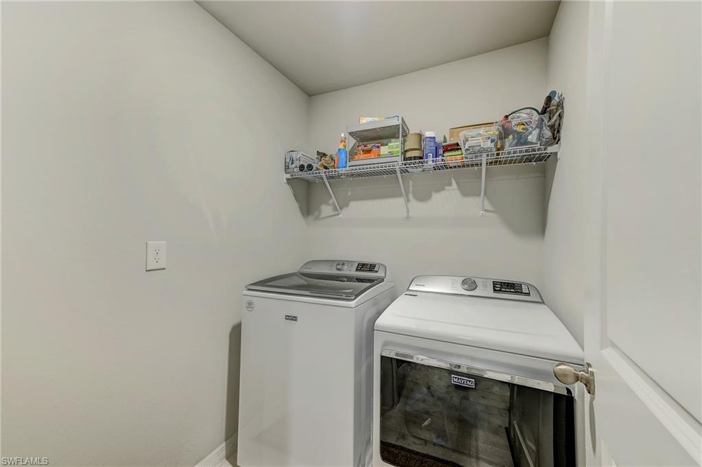 Laundry room with a white washer and dryer beneath a wire shelf of household supplies.