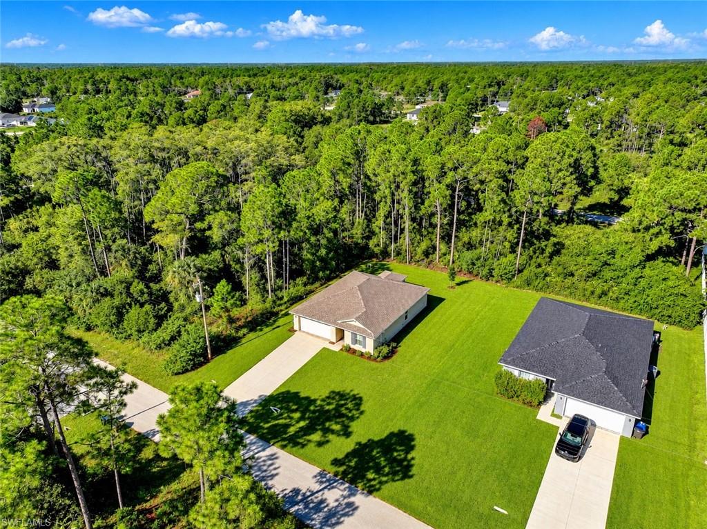 Aerial view of a single-story home with a broad lawn and dense trees behind it.