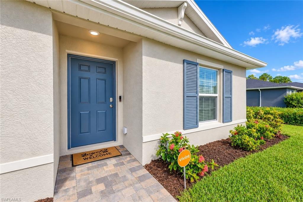 Home entrance with a blue front door, paver walkway, and window with blue shutters.