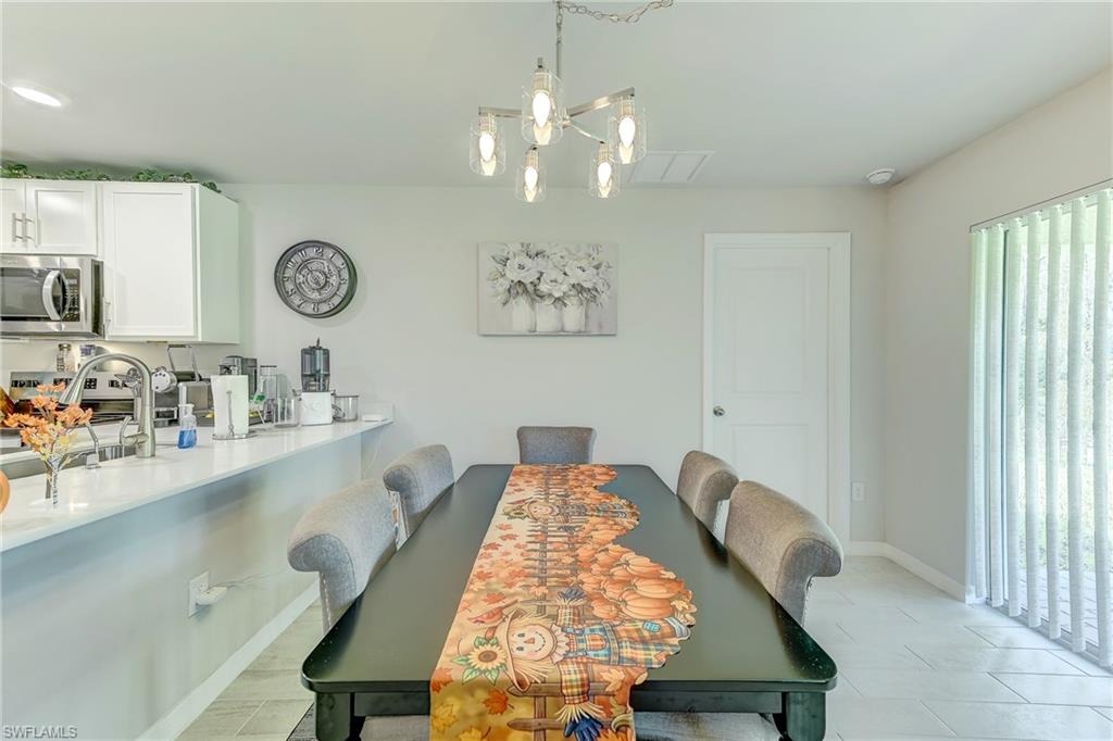 Dining area with a dark table, autumn-patterned runner, chandelier, and adjoining white kitchen.
