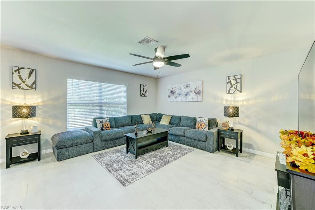 Living room with a gray sectional, patterned rug, black tables, and ceiling fan.