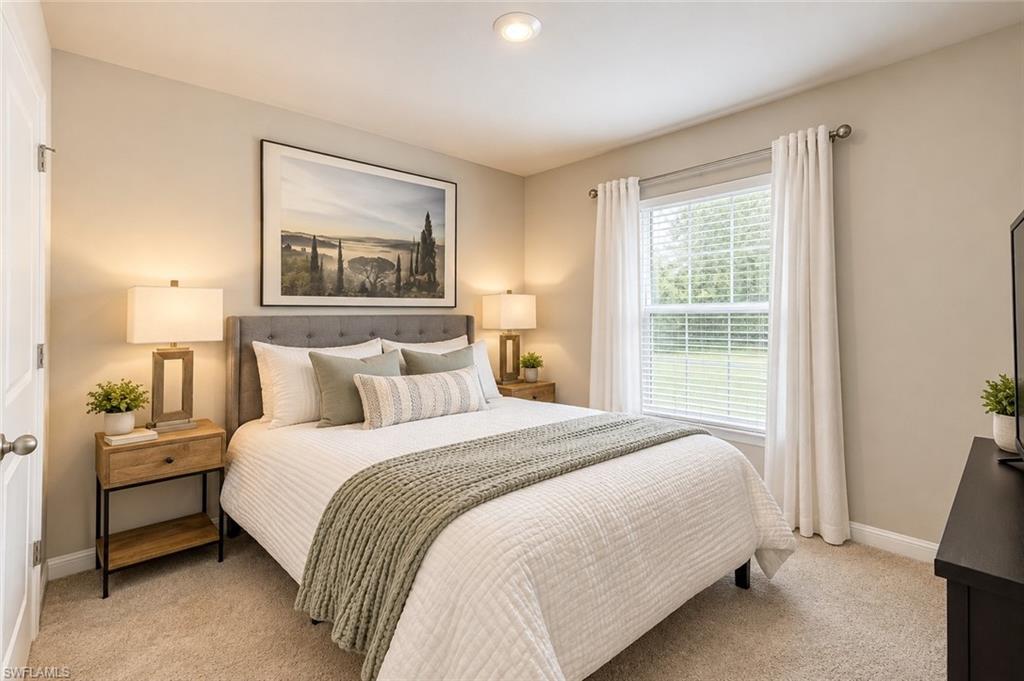 Staged bedroom with a large white bed, gray throw, matching bedside tables, and a bright curtained window.