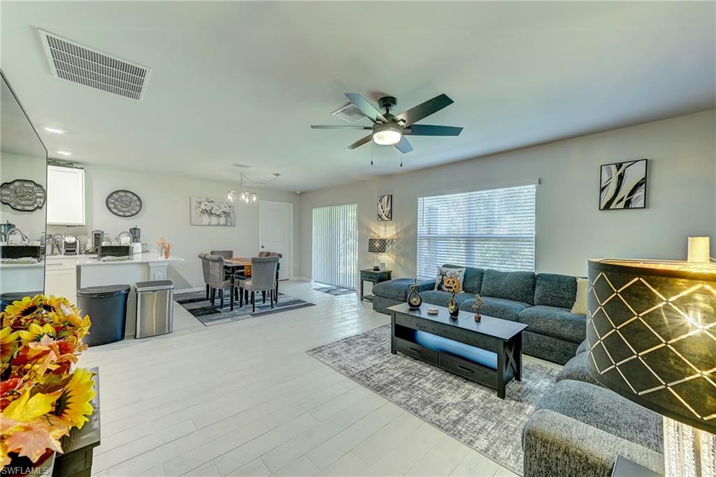 Open-plan living room with gray seating, dining area, kitchen, and large windows.